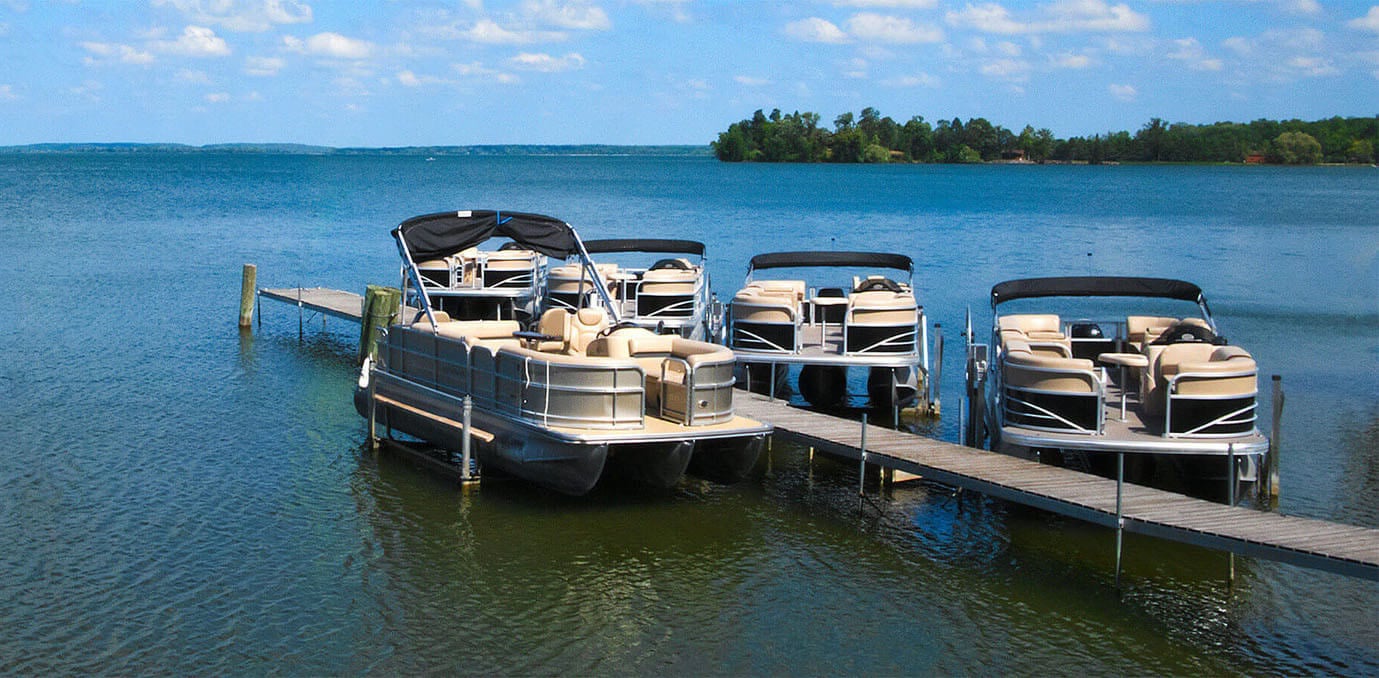 Four pontoon boats docked on a calm blue lake